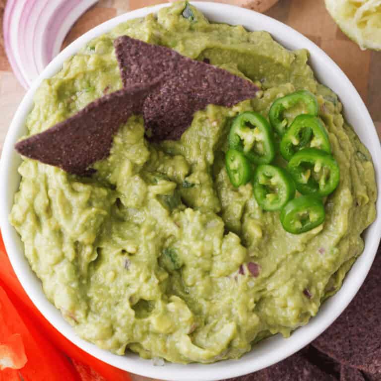 overhead closeup of guacamole in bowl with chips and sliced jalapenos accenting the top