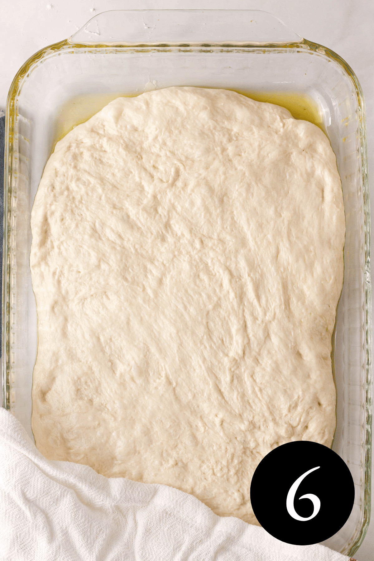 overhead image of focaccia dough gently stretched to edges of glass baking dish