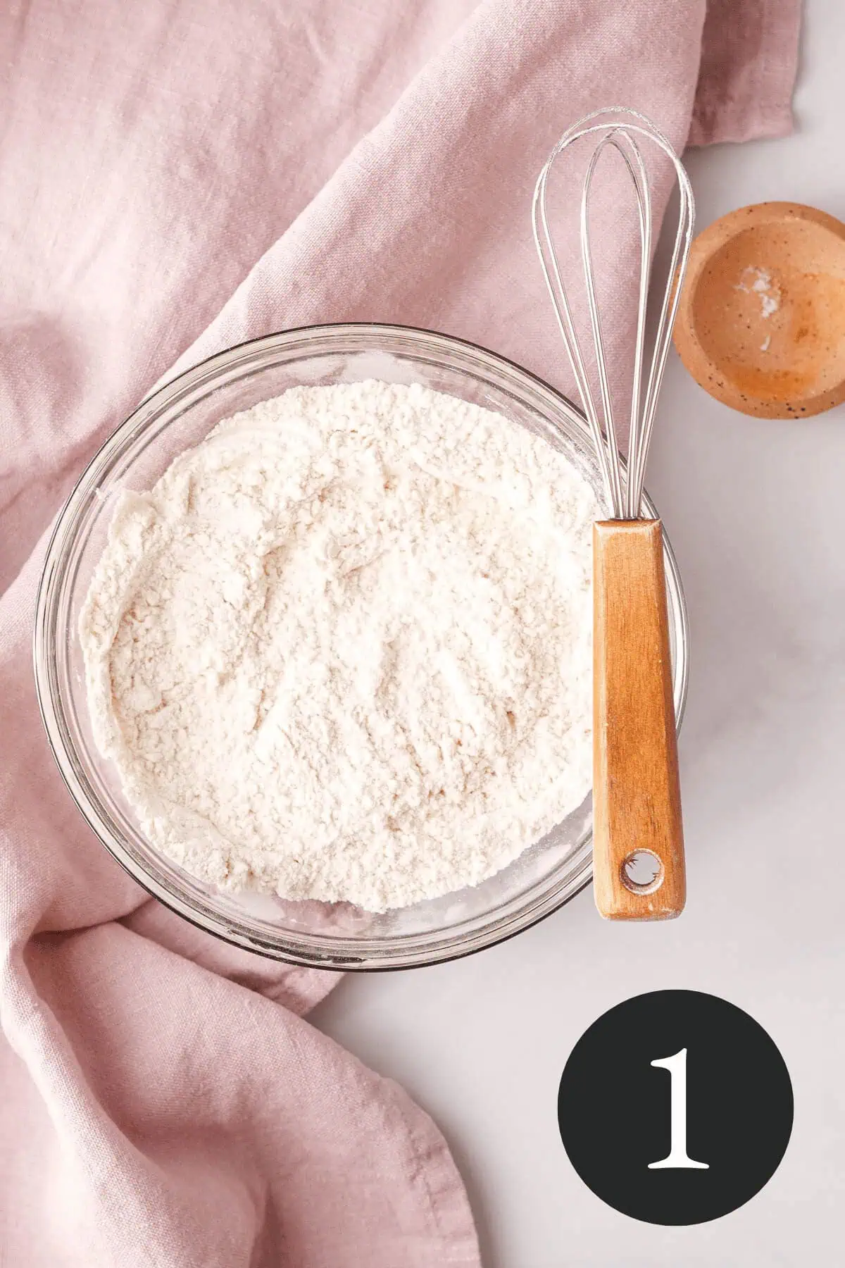 overhead image of dry ingredients whisked together with whisk resting across the top of the glass bowl
