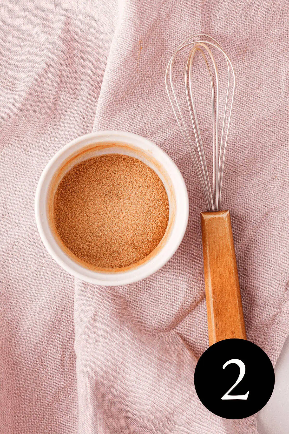 overhead image of granulated sugar whisked with ground cinnamon in small white bowl and whisk resting next to bowl