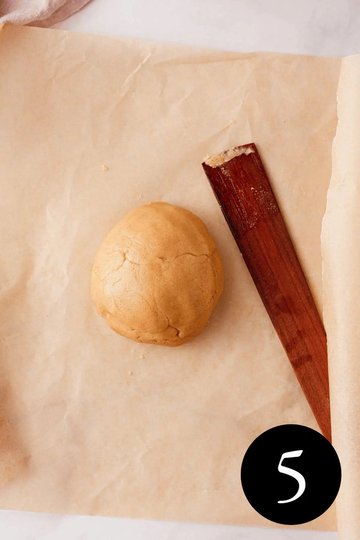 overhead image of cinnamon shortbread dough ball on parchment paper with spatula resting next to it