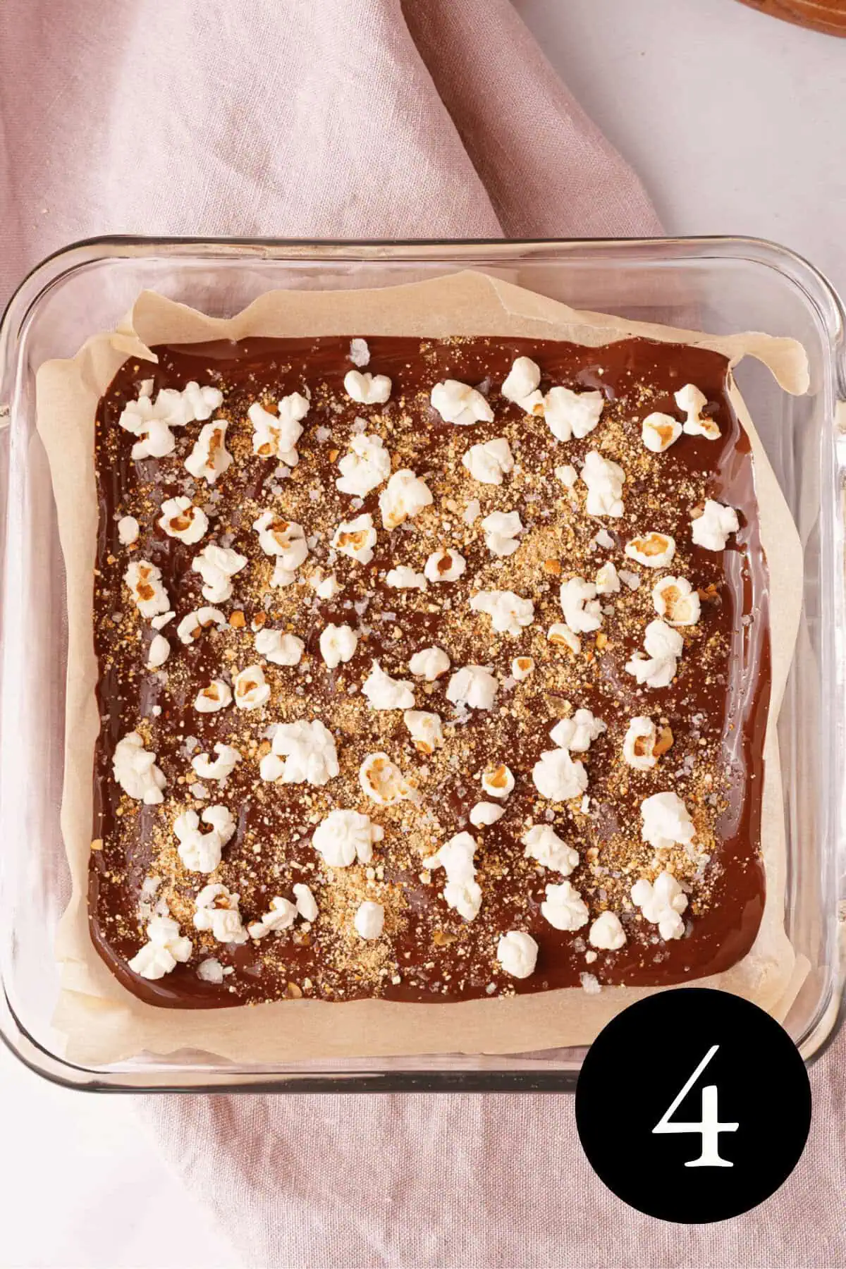 overhead image of popcorn bark in glass baking dish topped with popcorn and sea salt before setting in refrigerator
