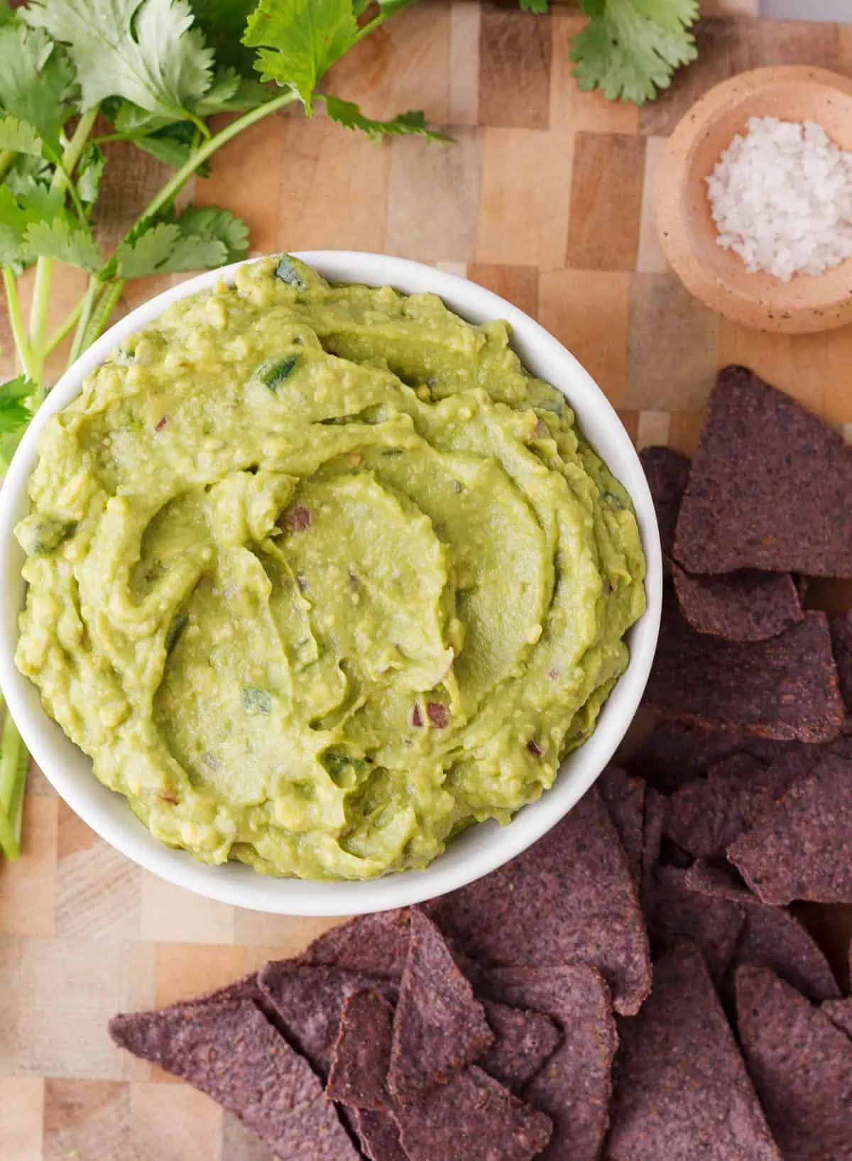 overhead image of guacamole in serving bowl framed by blue chips and cilantro on either side of the bowl