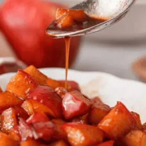 closeup of caramel sauce drizzling off spoon onto bowl of diced caramelized apples