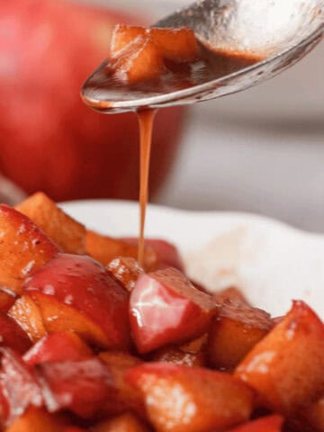 closeup of caramel sauce drizzling off spoon onto bowl of diced caramelized apples