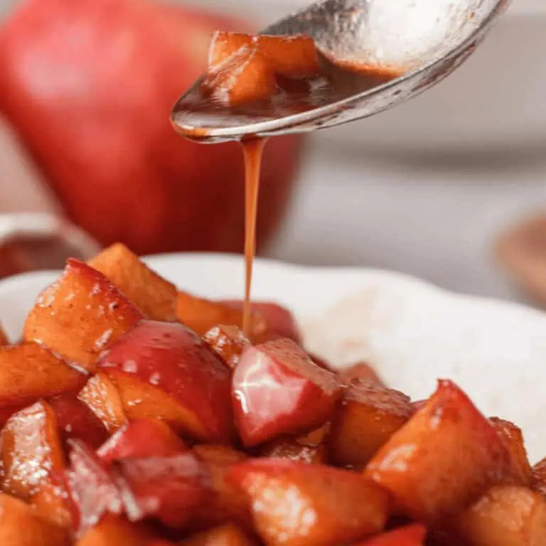 closeup of caramel sauce drizzling off spoon onto bowl of diced caramelized apples