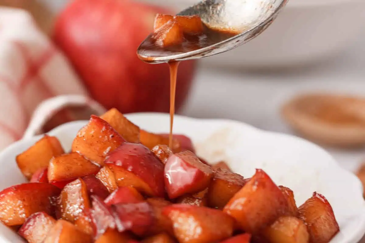 closeup of caramel sauce drizzling off spoon onto bowl of diced caramelized apples