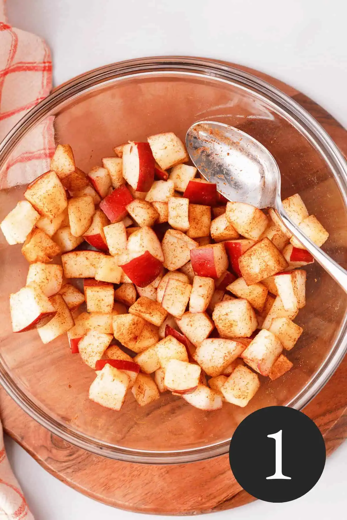 overhead image of diced apples coated in ground cinnamon in glass bowl with number one in the bottom right corner