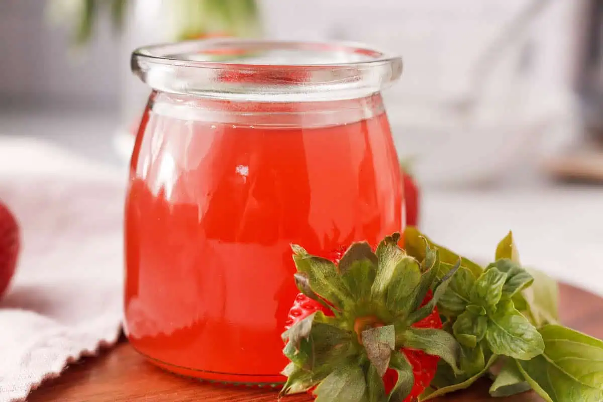 closeup of strawberry basil syrup in jar with strawberry top and basil propped against side of jar