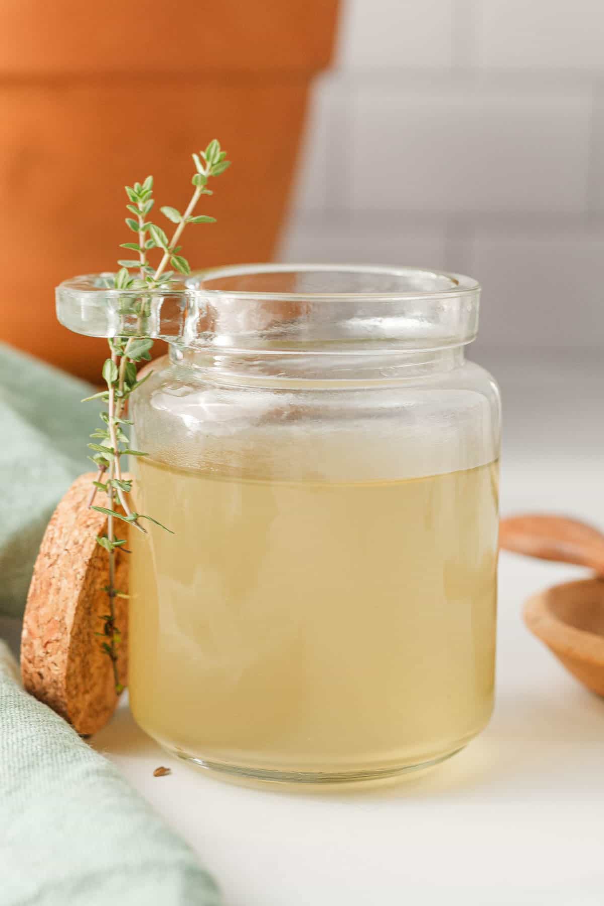 closeup of thyme simple syrup in glass jar with thyme sprigs on the side and terra cotta planter in the background
