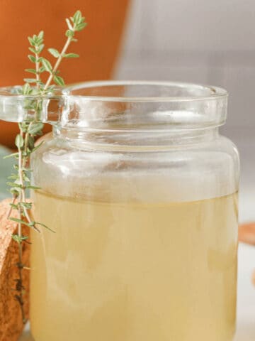 closeup square image of thyme simple syrup in glass jar with thyme sprigs on the side