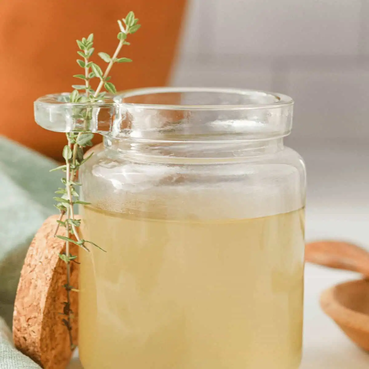 closeup square image of thyme simple syrup in glass jar with thyme sprigs on the side
