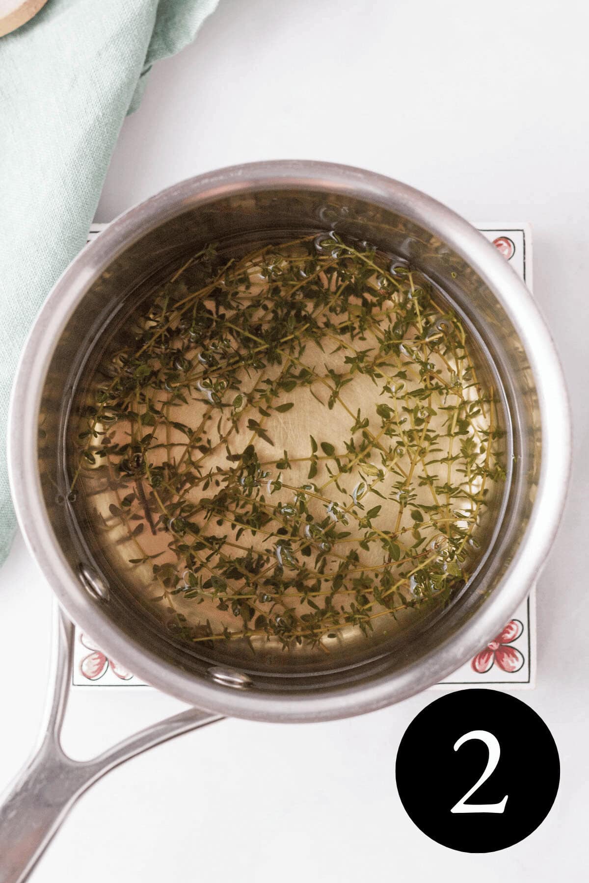 overhead image of fresh thyme sprigs in saucepan after simmering to show yellow tint to the liquid