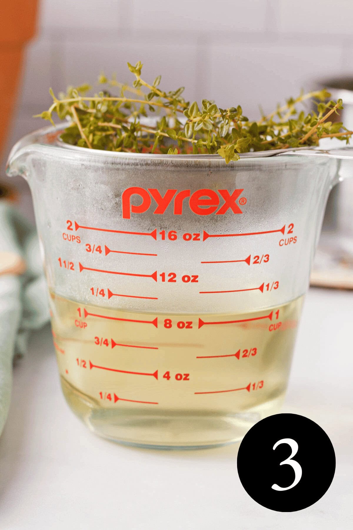 side image of pyrex large measuring up with fine mesh strainer resting on top holding fresh thyme sprigs