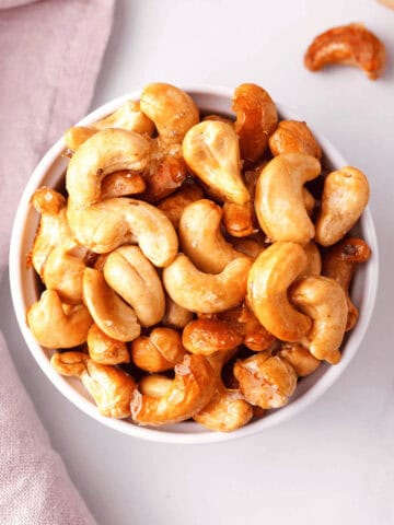 overhead closeup of maple roasted cashews in small serving bowl with individual cashews spaced on the counter