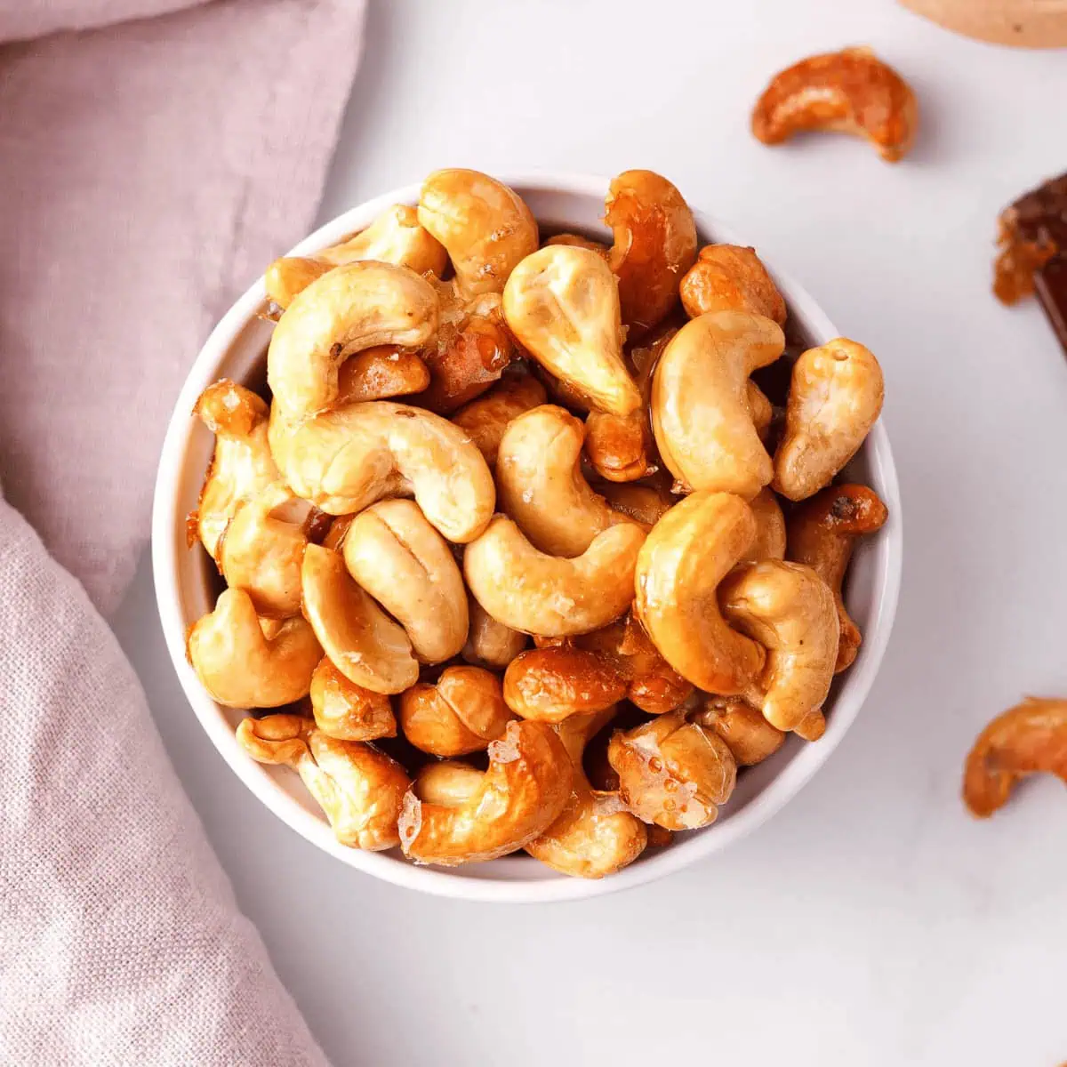 overhead closeup of maple roasted cashews in small serving bowl with individual cashews spaced on the counter