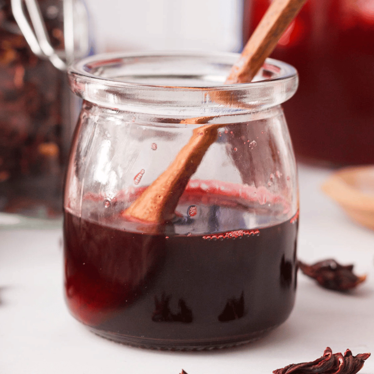 closeup of hibiscus simple syrup in glass jar with wooden spoon resting in jar
