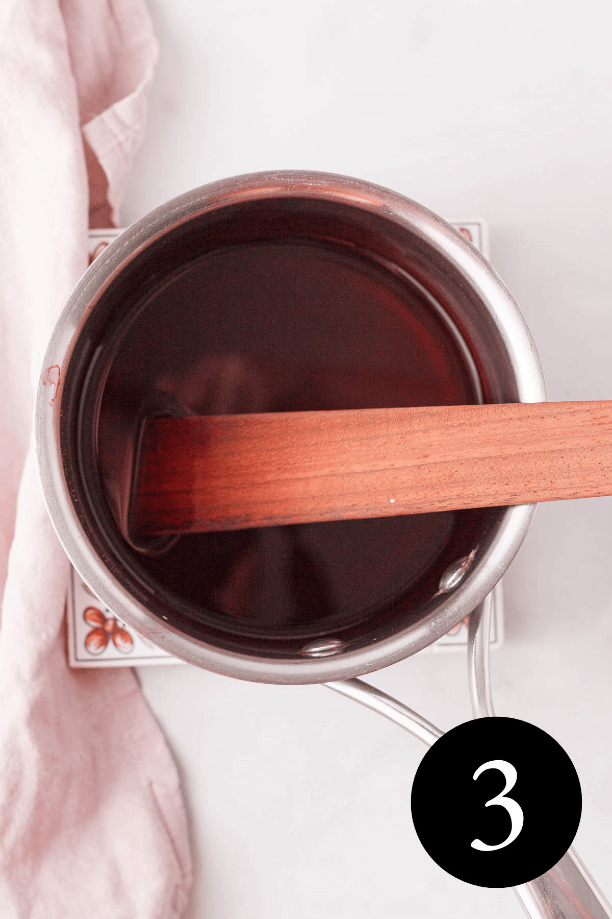 overhead image of hibiscus simple syrup in saucepan after stirring in stevia and arrowroot with spatula resting in pan