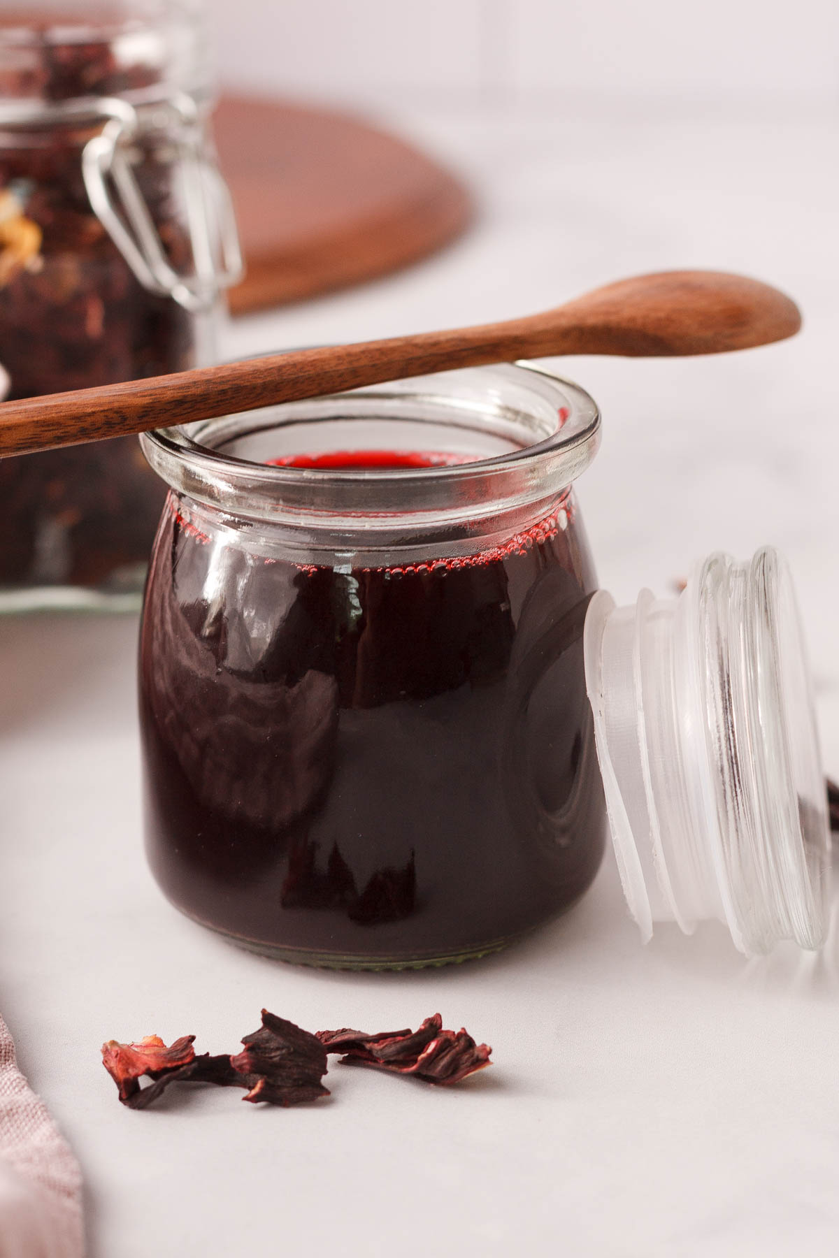 closeup of hibiscus simple syrup in small glass jar with wood spoon resting across the top