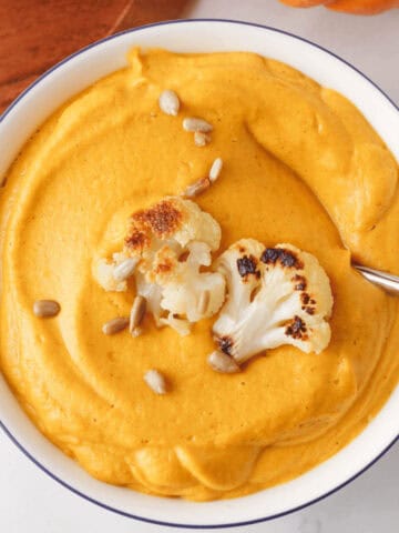 overhead image of cauliflower pumpkin soup in bowl with spoon resting along the edge