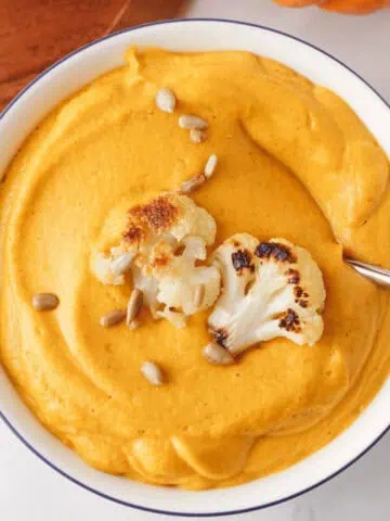 overhead image of cauliflower pumpkin soup in bowl with spoon resting along the edge