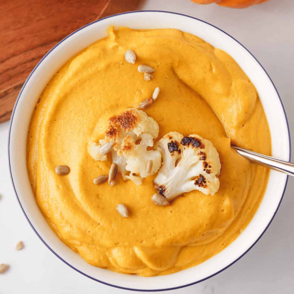 overhead image of cauliflower pumpkin soup in bowl with spoon resting along the edge