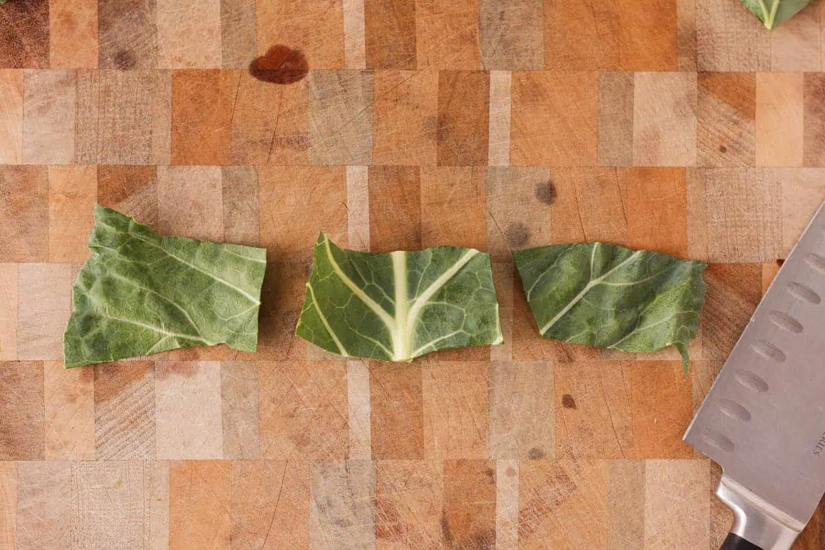 a strip of collard green leaves cut into three pieces on cutting board