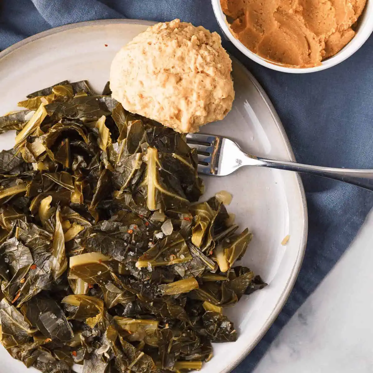 overhead image of miso collard greens on plate with beer biscuit and a container of white miso peeking in from the top right corner