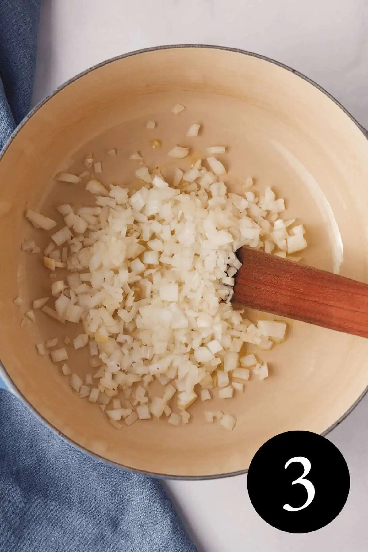 overhead image of diced onion and olive oil sautรฉing in Dutch oven with wooden spatula propped in the pot and number five in the bottom right corner