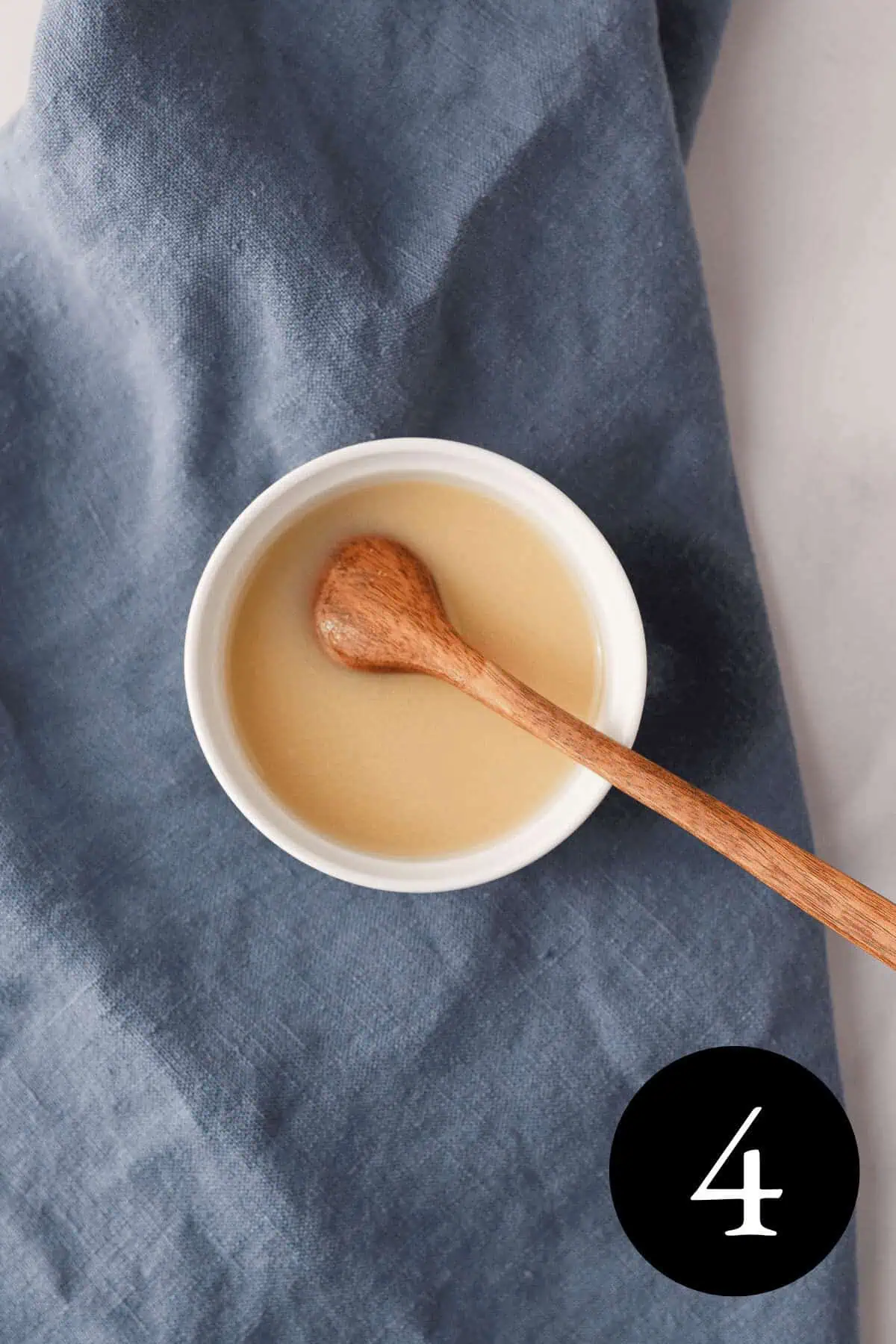 overhead image of miso dissolved in water with wooden spoon resting in small white bowl and number 4 in bottom right corner