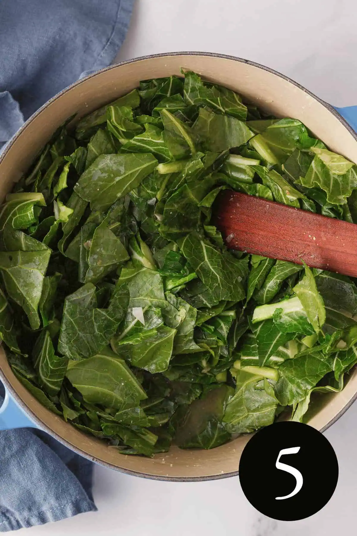 overhead image of collard greens in Dutch oven with wooden spatula resting in pot with number five in bottom right corner