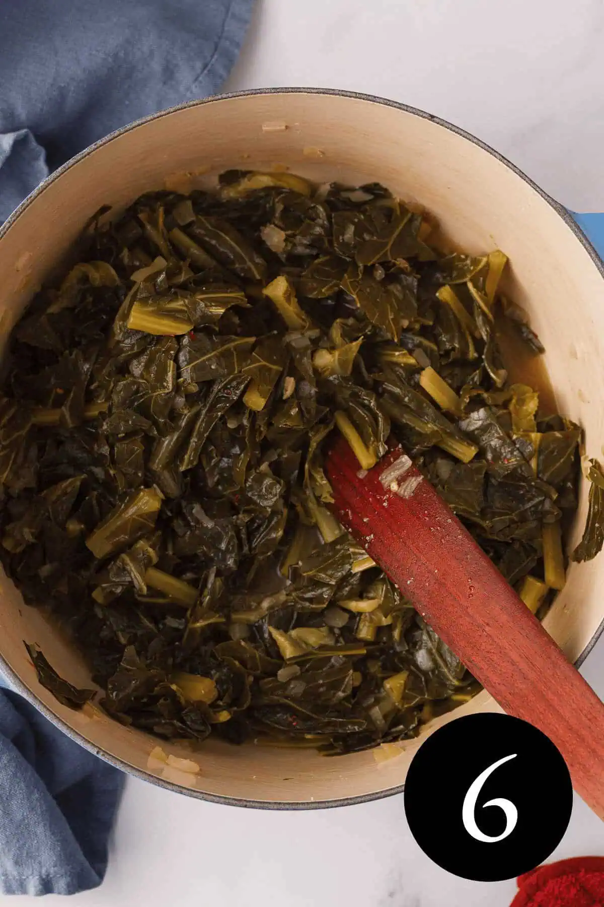 overhead image of cooked miso collard greens in Dutch oven with wooden spatula resting in pot and number six in bottom right corner