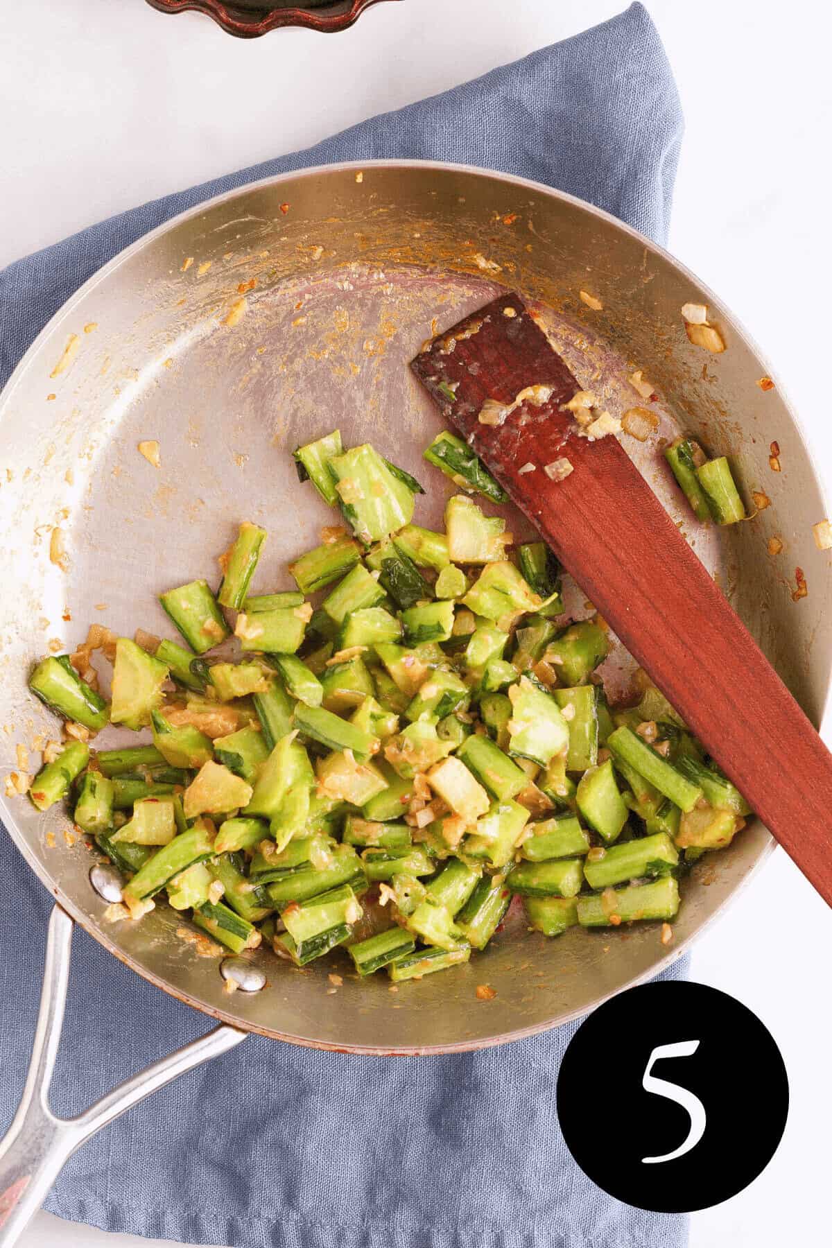 overhead image of sautéed collard green stems in miso sauce with wooden spatula resting in skillet and number five in the bottom right corner
