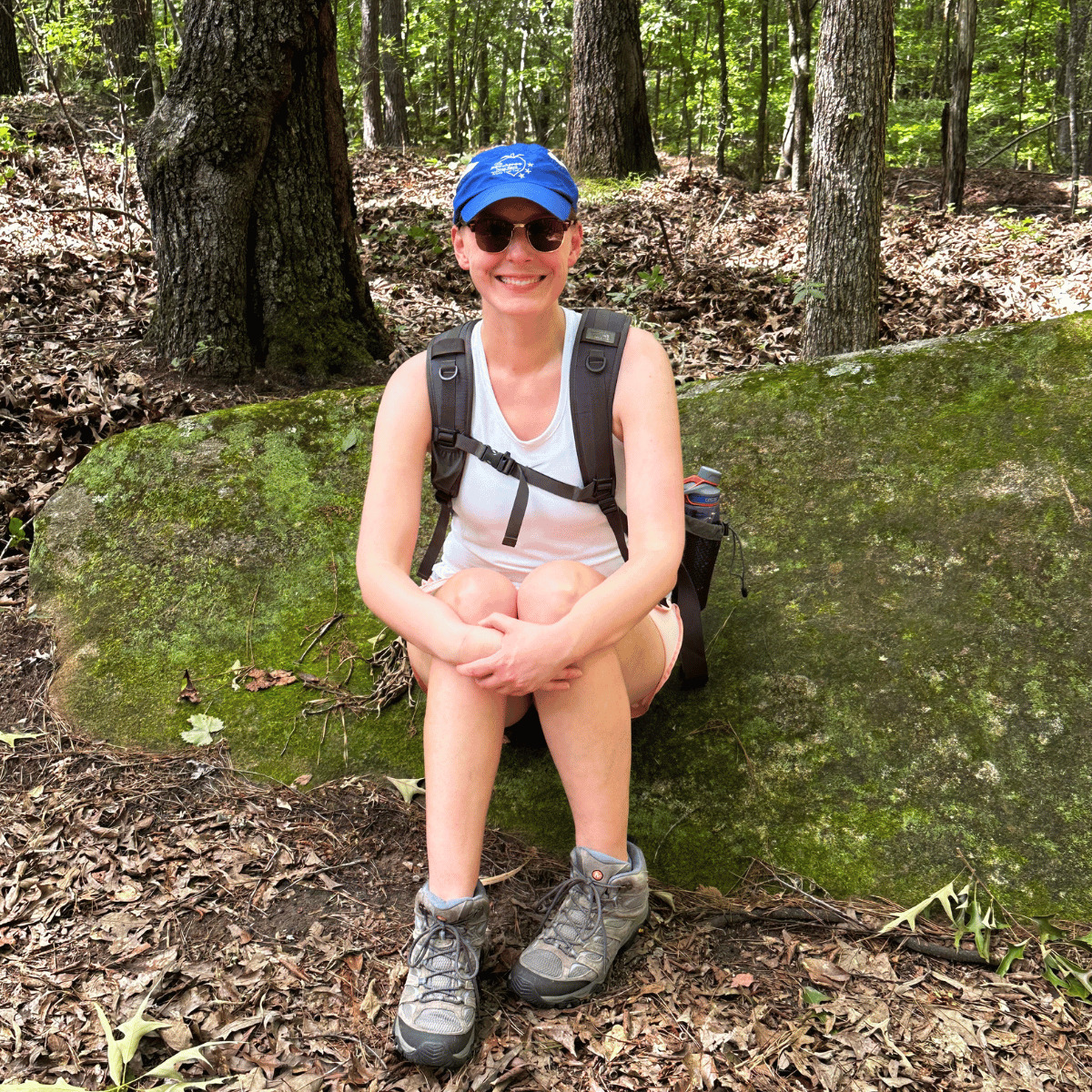 melanie sitting on a large rock while hiking a trail
