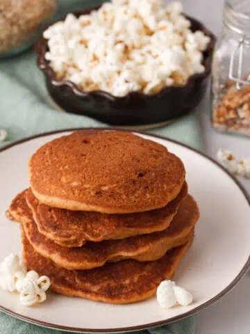 angled image stacked popcorn pancakes on plate with popped popcorn and unpopped kernels in the background