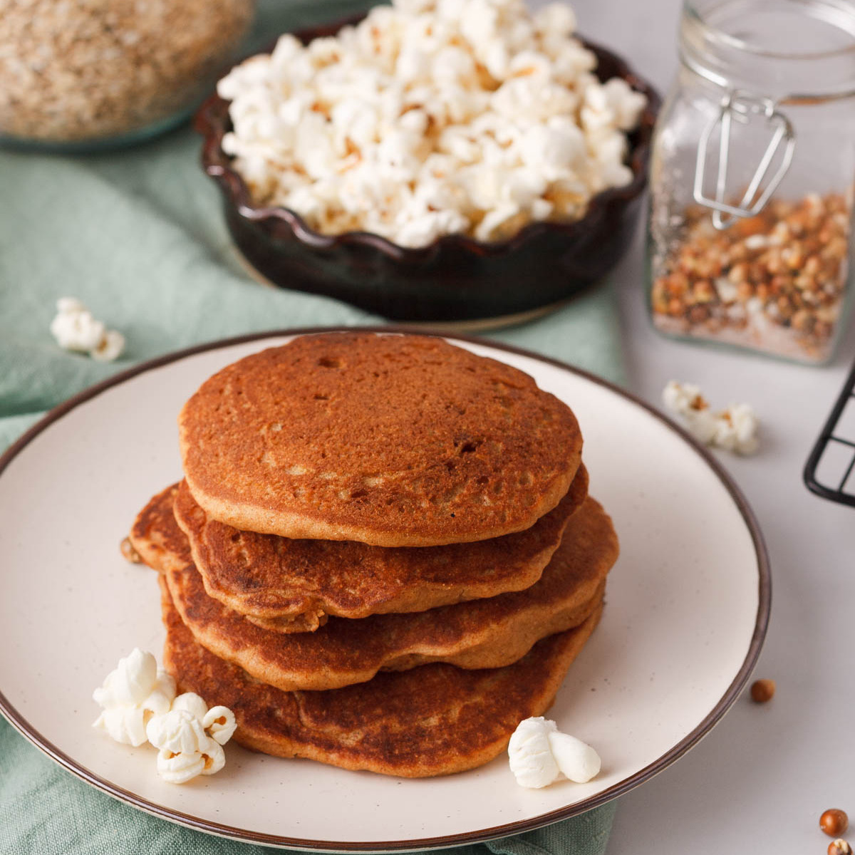 angled image stacked popcorn pancakes on plate with popped popcorn and unpopped kernels in the background