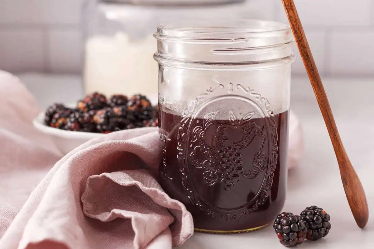 closeup of blackberry simple syrup in mason jar with wooden spoon propped against side and ingredients in the background
