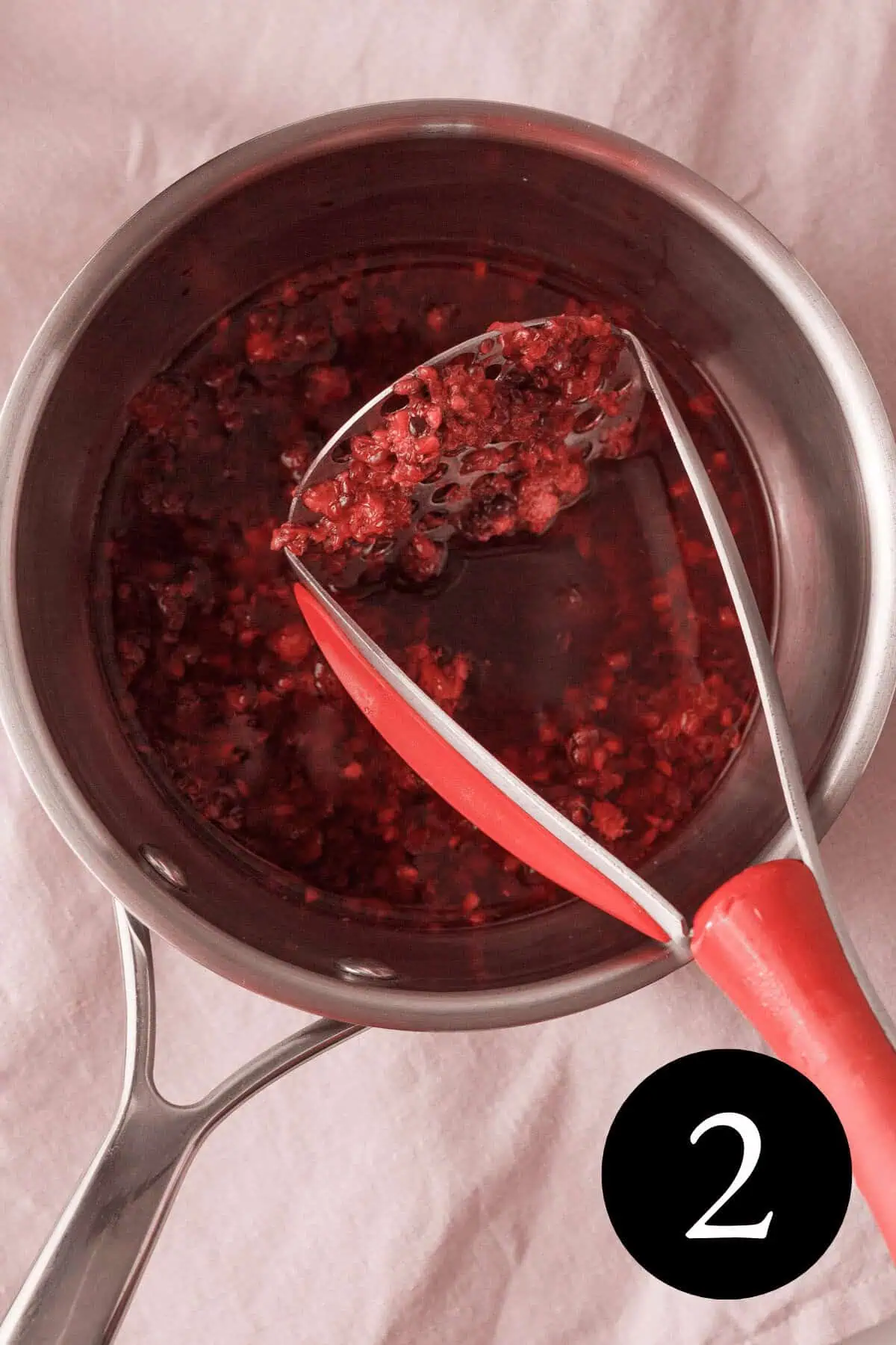 overhead image of blackberries mashed and potato masher propped against side with number two in bottom right corner