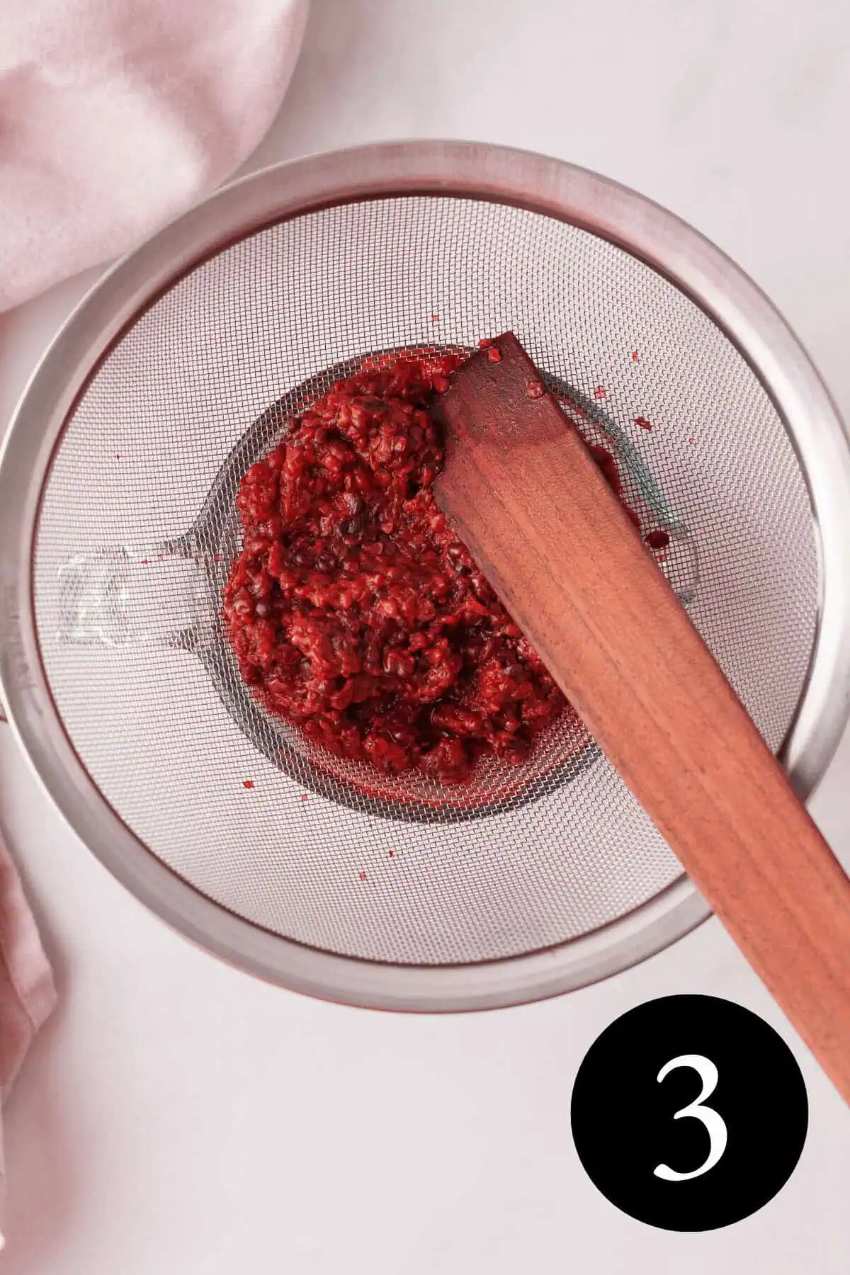 overhead image of blackberry pulp in strainer with wood spatula and number three in bottom right corner