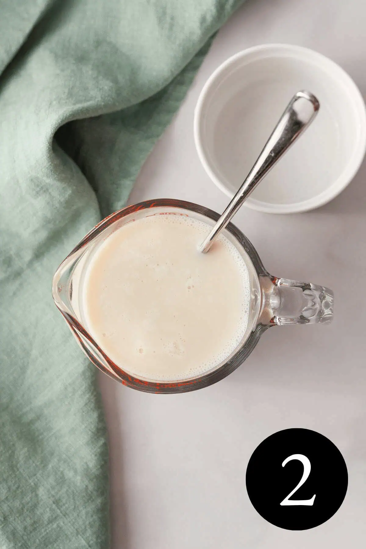 overhead image of vegan buttermilk in liquid measuring cup with empty white bowl next to it and number two in bottom right corner