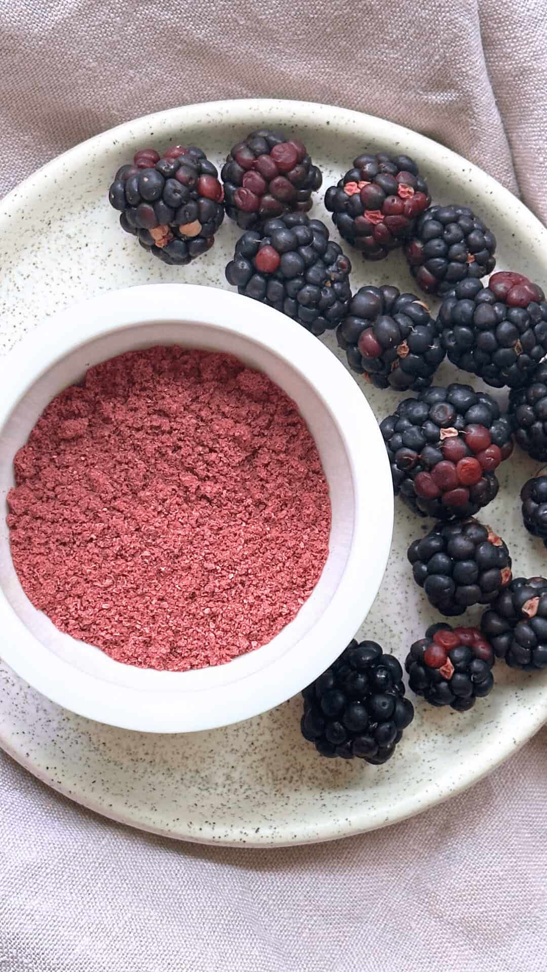 overhead image of blackberry powder in small white bowl on plate accented by fresh blackberries