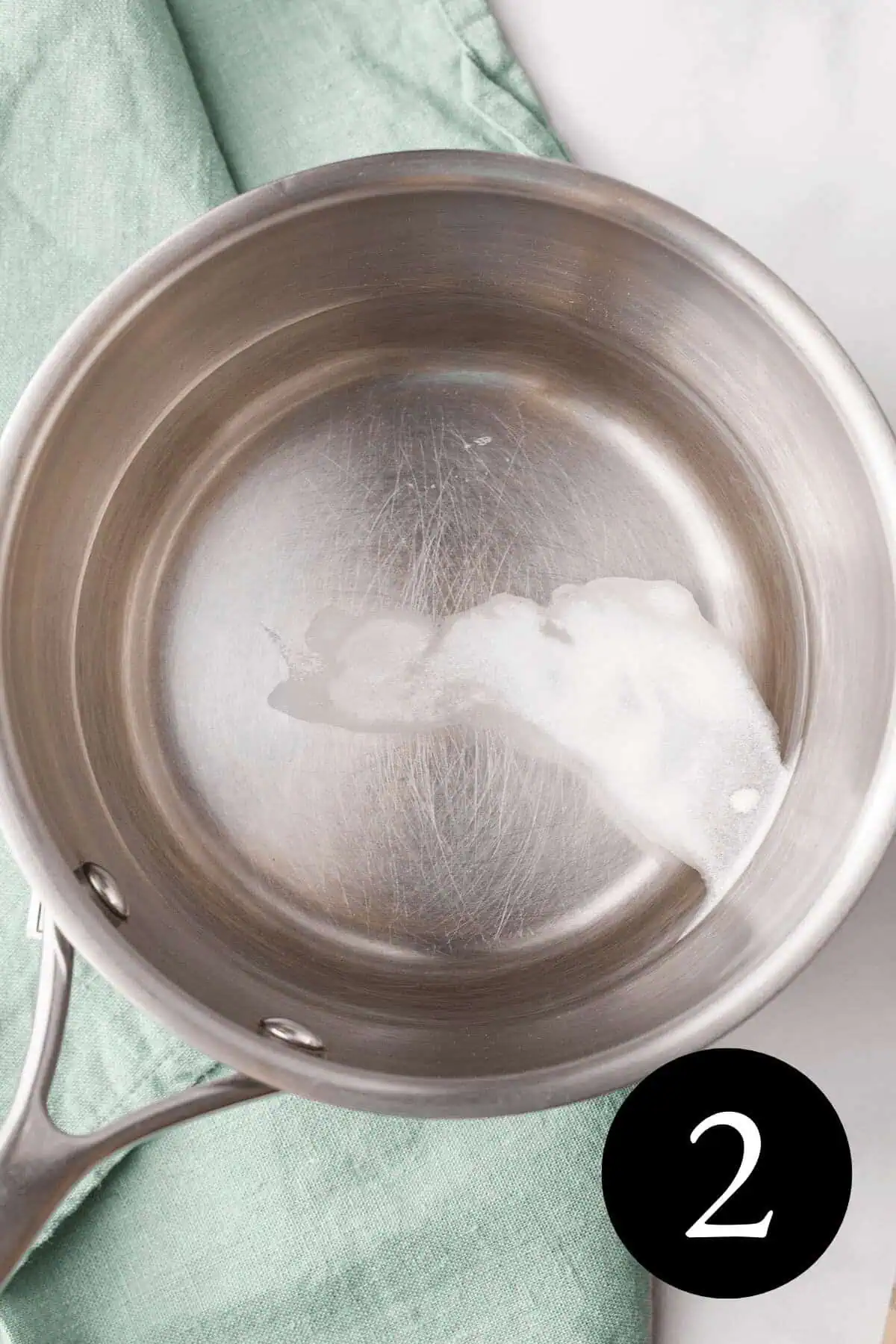 overhead image of liquid in saucepan with stevia powder before stirring and number two in bottom right corner