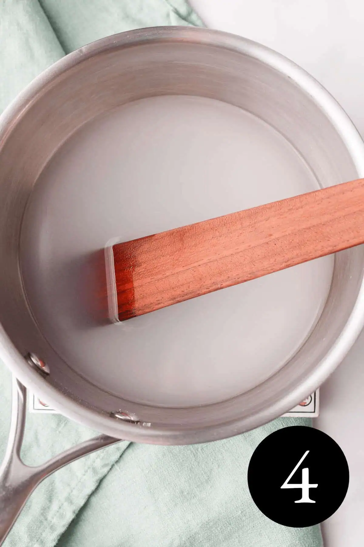 overhead image of liquid in saucepan cloudy in appearance with wooden spatula and number four in the bottom right corner