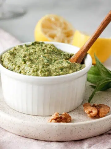 closeup of vegan basil pesto in white bowl surrounded by ingredients
