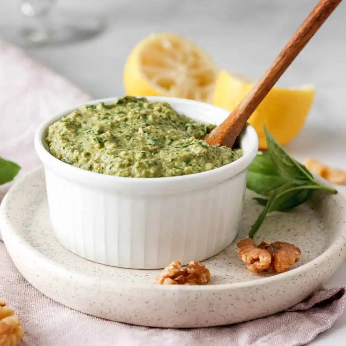 closeup of vegan basil pesto in white bowl surrounded by ingredients