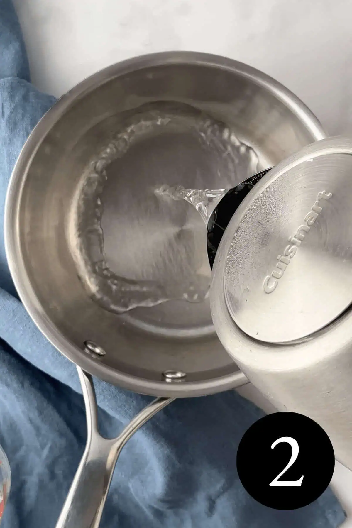 overhead image of boiling water in kettle pouring into saucepan with number two in bottom right corner