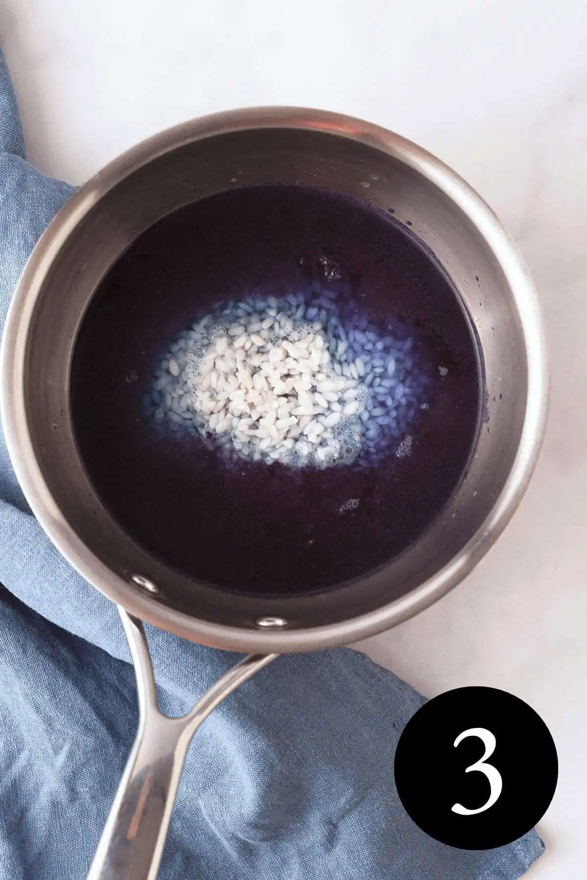 overhead image of rice in blue liquid in saucepan with number three in bottom right corner