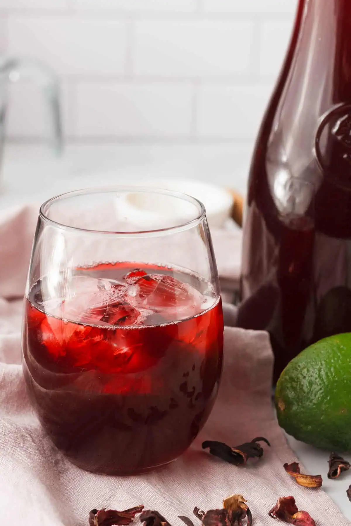 hibiscus tea with cinnamon in glass next to lime and carafe with rest of liquid