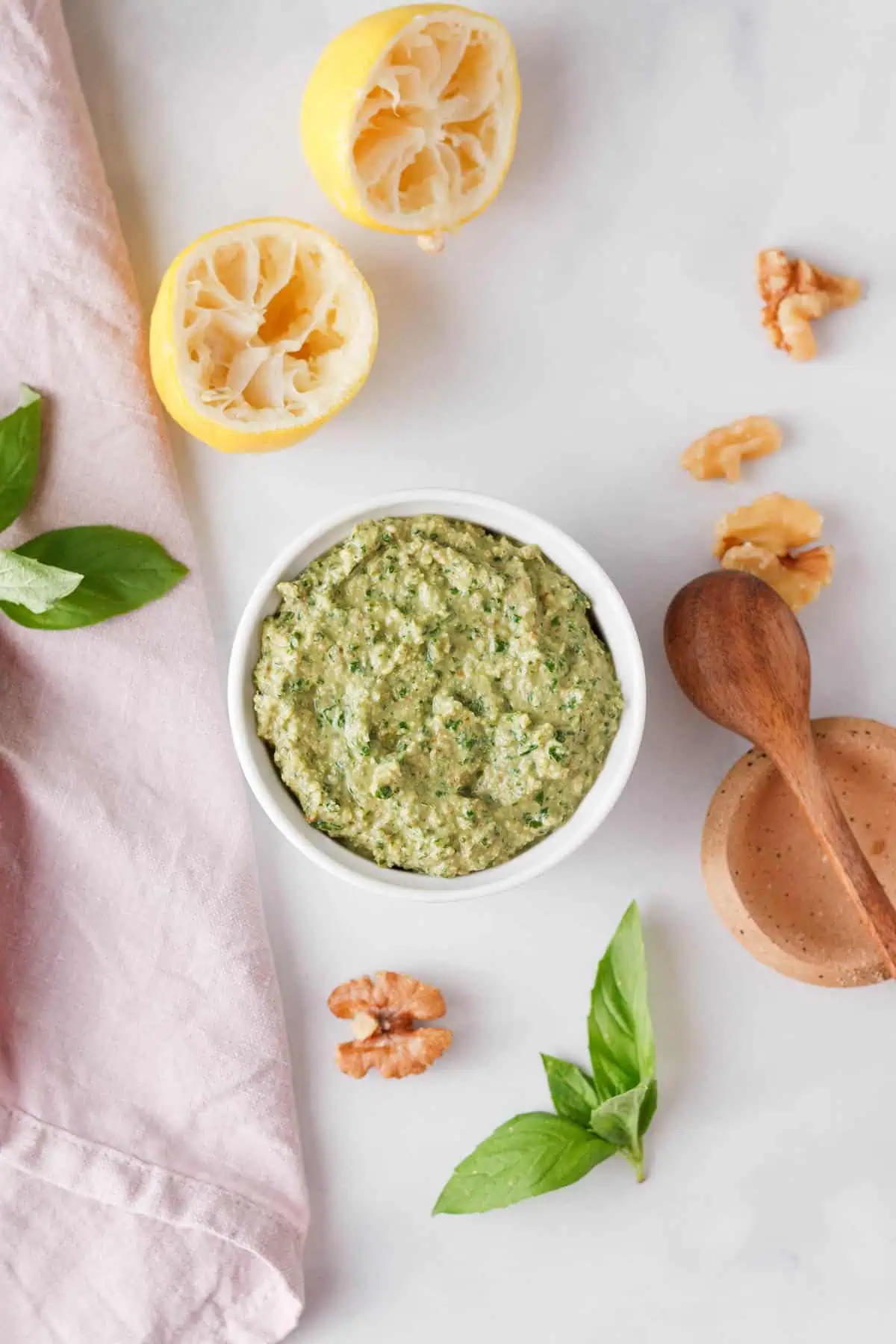 overhead image of vegan basil pesto in bowl on counter next to used ingredients