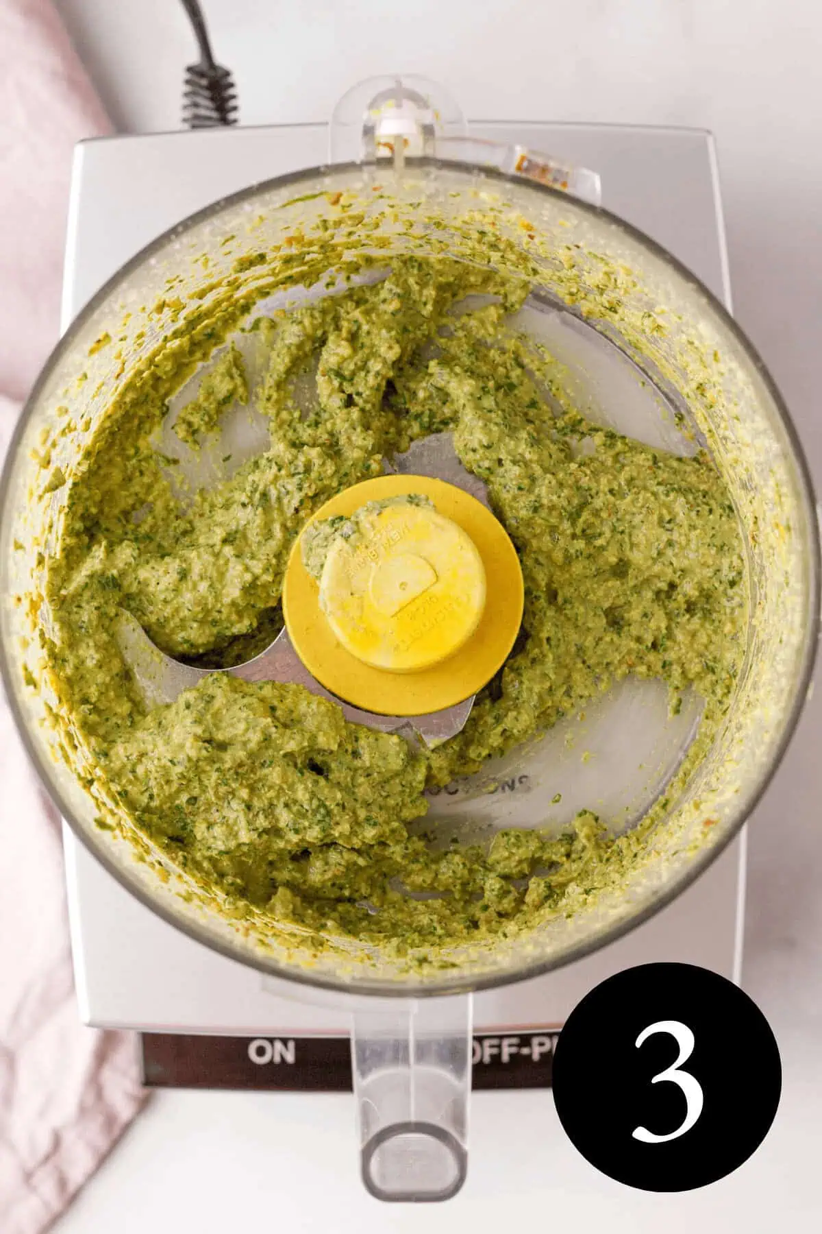 overhead image of vegan basil pesto in bowl of food processor with number three in bottom right corner
